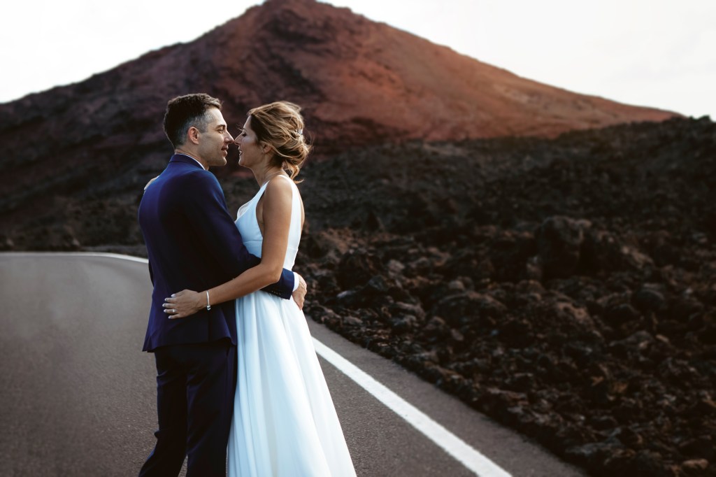 Couple kissing in front of a red volcanic mountain in Lanzarote, captured by a wedding and elopement photographer