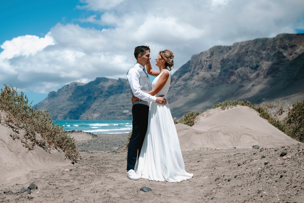 Bridal couple hugging and gazing at each other on Famara Beach - a romantic setting captured by a wedding photographer in Lanzarote