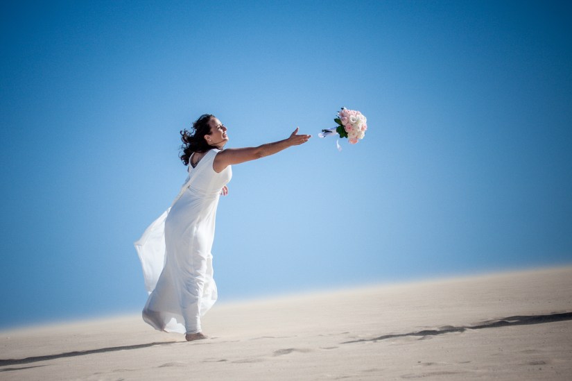 Rainbow wedding in the dunes - vibrant lesbian couple twirling with Atlantic Ocean backdrop
