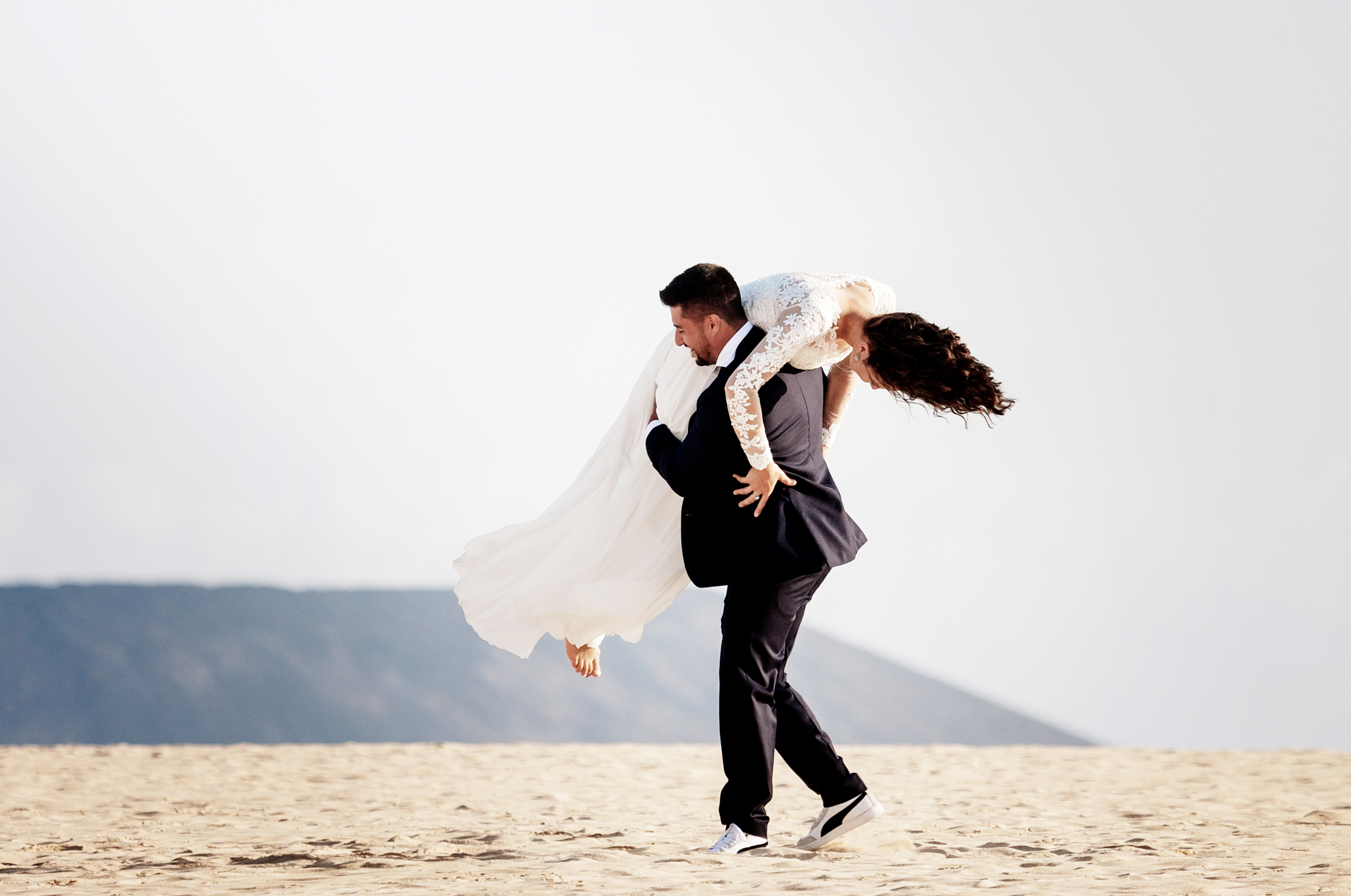 Groom holds bride on his shoulder like a bag of potatoes in the beach of Fuerteventura