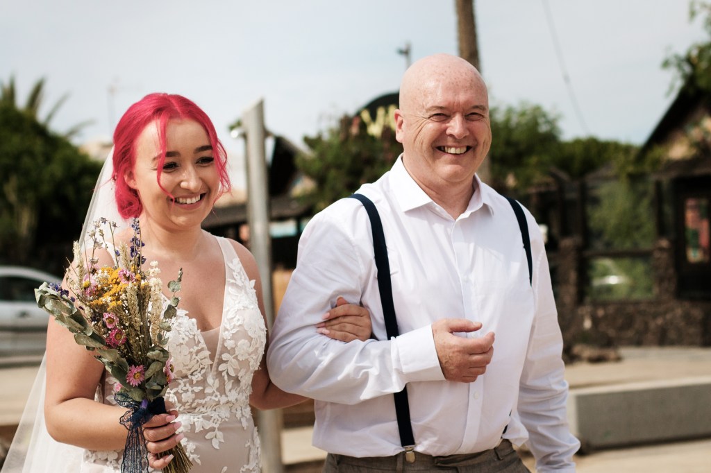 Capture a heartwarming moment of a father walking his daughter down the aisle with our expert photography. A touching photo of a bride and her father looking towards the Fuerteventura wedding photographer during their Corralejo wedding ceremony. Our professional photographer captures every detail with precision and artistry