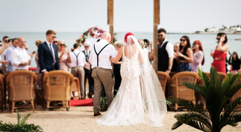 Budget-friendly wedding photography excellence - close-up of celebrant placing flowers in couple's hands at Corralejo beach ceremony