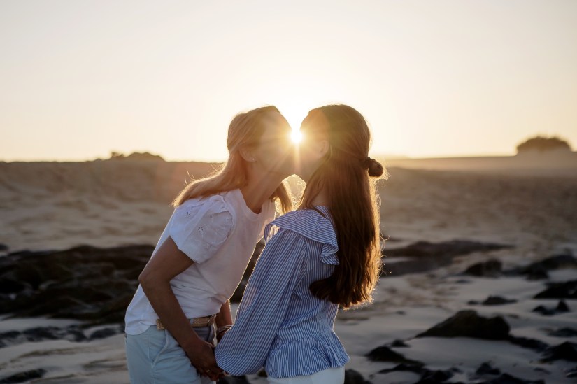 Mother is kissing her daughter and the sunray is between them in a golden hour in the Sand Dunes of Corralejo in Fuerteventura