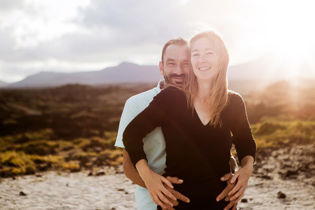 Lanzarote wedding photographer captures the beauty of love and nature - couple hugging in volcanic area at sunset, with direct eye contact to the camera. Trust Andrius Tekorius from photofuerte, a highly experienced wedding photographer in Lanzarote, to capture your special day
