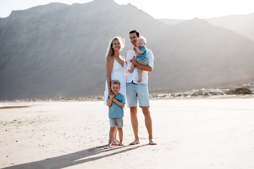 Familie am schönen Strand von Famara auf Lanzarote, mit der Sonne, die hinter dem Berg scheint. Aufgenommen von einem Familienfotografen in Lanzarote