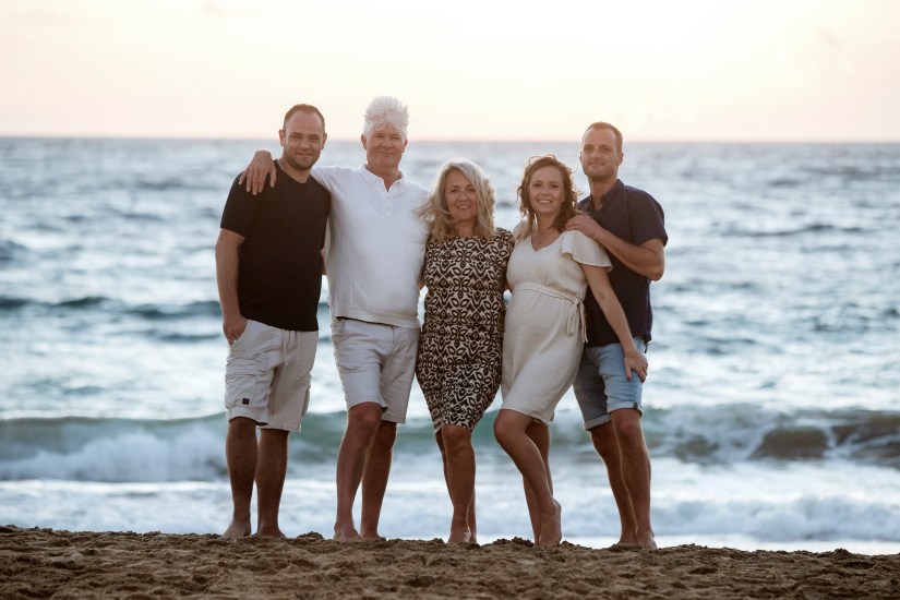 Gouden uurtje familiefotoshoot - dierbaren omhelzen elkaar met de dramatische kliffen van Playa Papagayo op de achtergrond, vastgelegd door topfotograaf