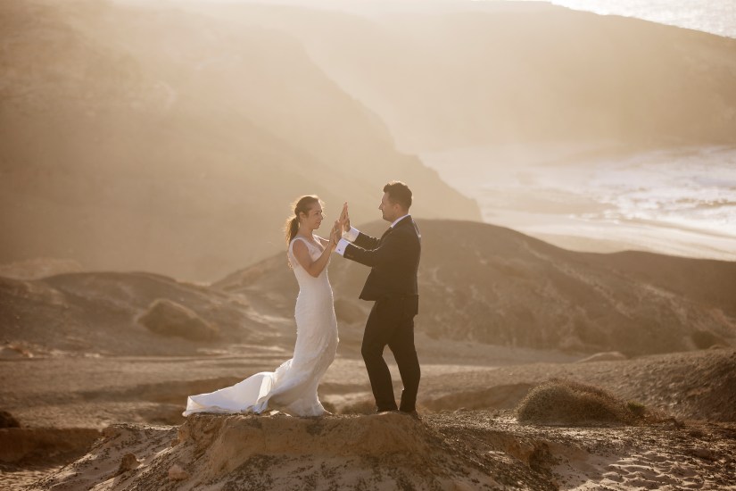Fotografia ślubna na wulkanicznej plaży – sylwetki młodej pary na tle czarnego piasku o zachodzie słońca
