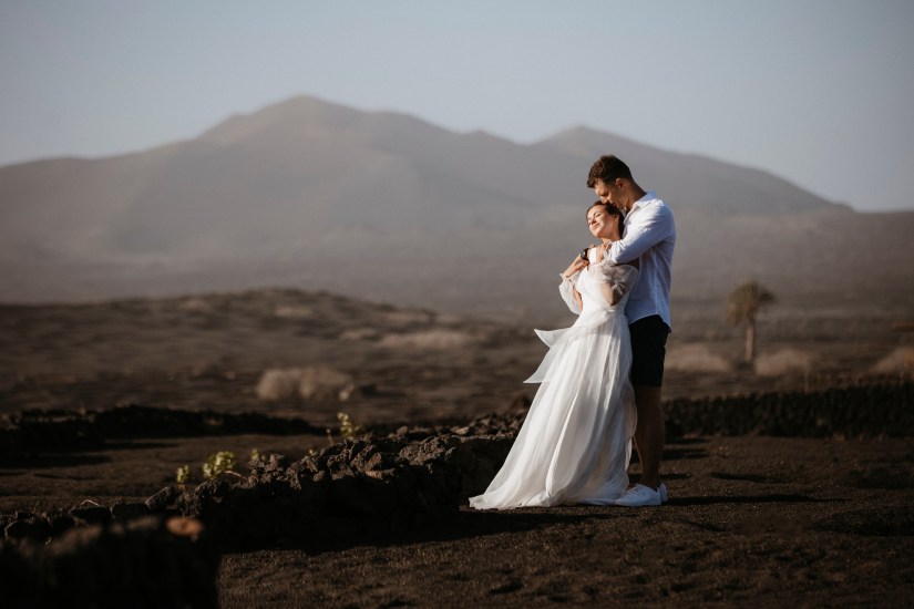 Bruid en groom omhelzen elkaar in het vulkanische landschap van La Geria, Lanzarote – trouwfotograaf voor avontuurlijke huwelijken