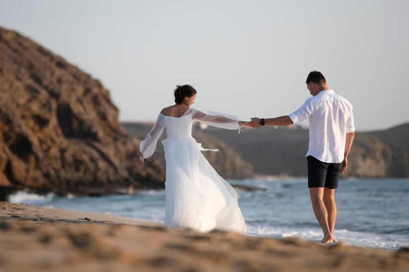 Romantische omhelzing van newlyweds op het goudgele zand van Playa Papagayo - Lanzarote trouwfotograaf